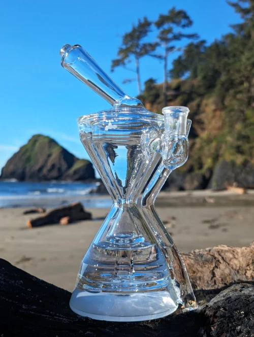 Glass water pipe on beach with clear sky.